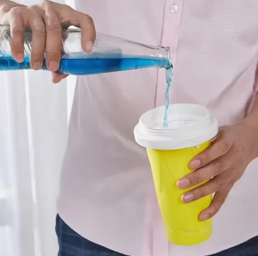 Person pouring blue liquid from a bottle into a yellow cup with a white lid.